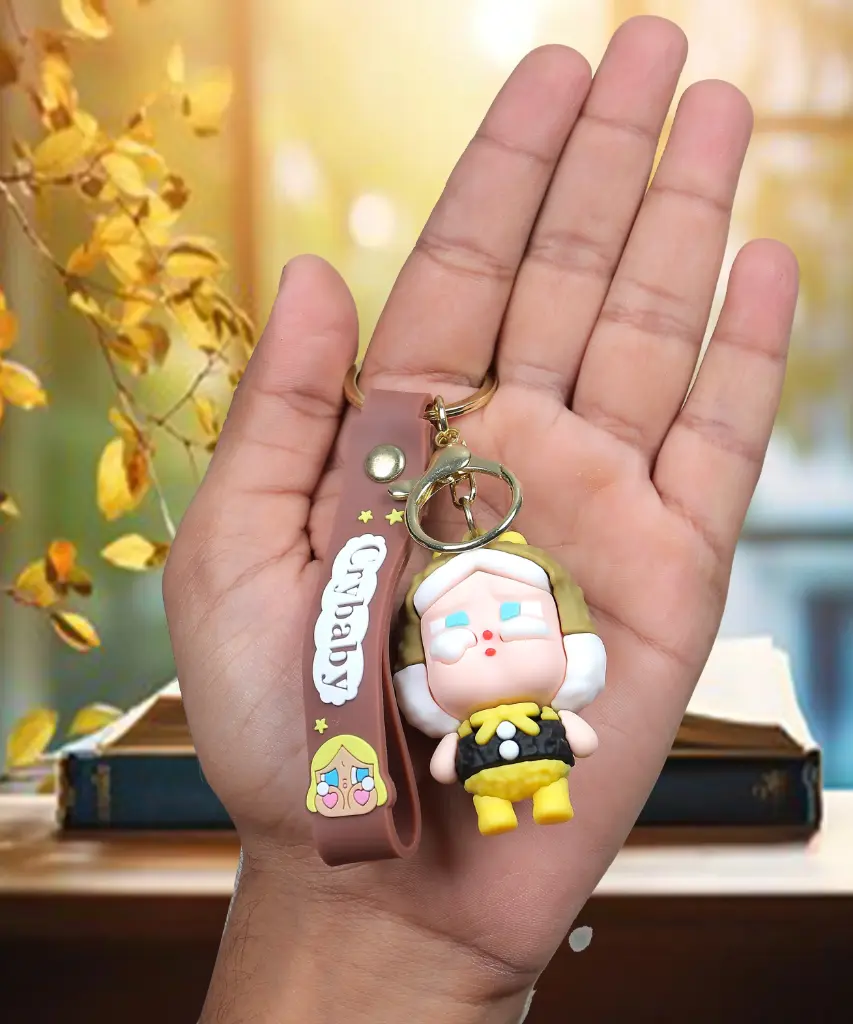 Brown Crybaby Doll Figure Keychain with Yellow Hood | "Crybaby" Logo Wrist Strap Accessory | Trendy Collectible Key Ring