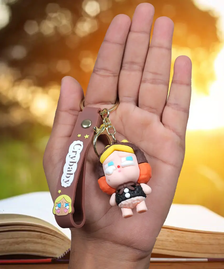 Red Brown Crybaby Doll Figure Keychain with Yellow Hood | "Crybaby" Logo Wrist Strap Accessory | Trendy Collectible Key Ring